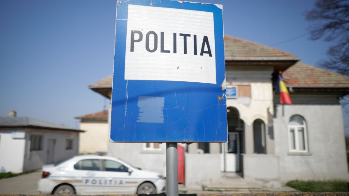 Fotografie cu un indicator pe care scrie „POLITIA” în fața unei case și o mașină de poliție parcată în fundal.