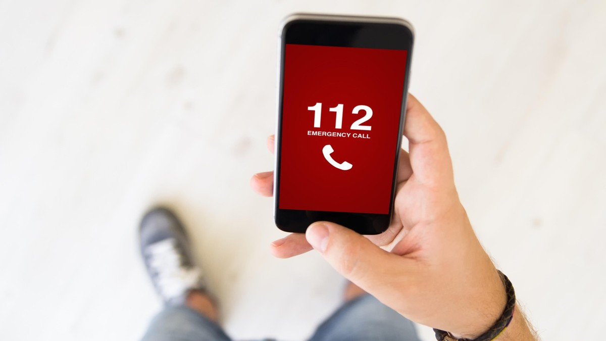 Bărbat care ține în mână un telefon pe ecranul căruia este afișat numărul unic de urgență 112.