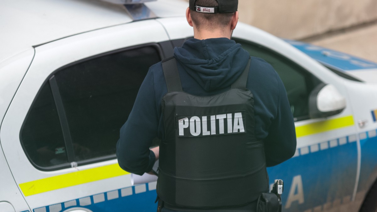 Un polițist cu vestă antiglonț, în timp ce încearcă să deschidă ușa unei mașini de Poliție