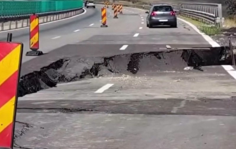 O porțiune de asfalt surpată pe o autostradă, unde zona afectată este semnalizată cu balize rutiere temporare de avertizare.