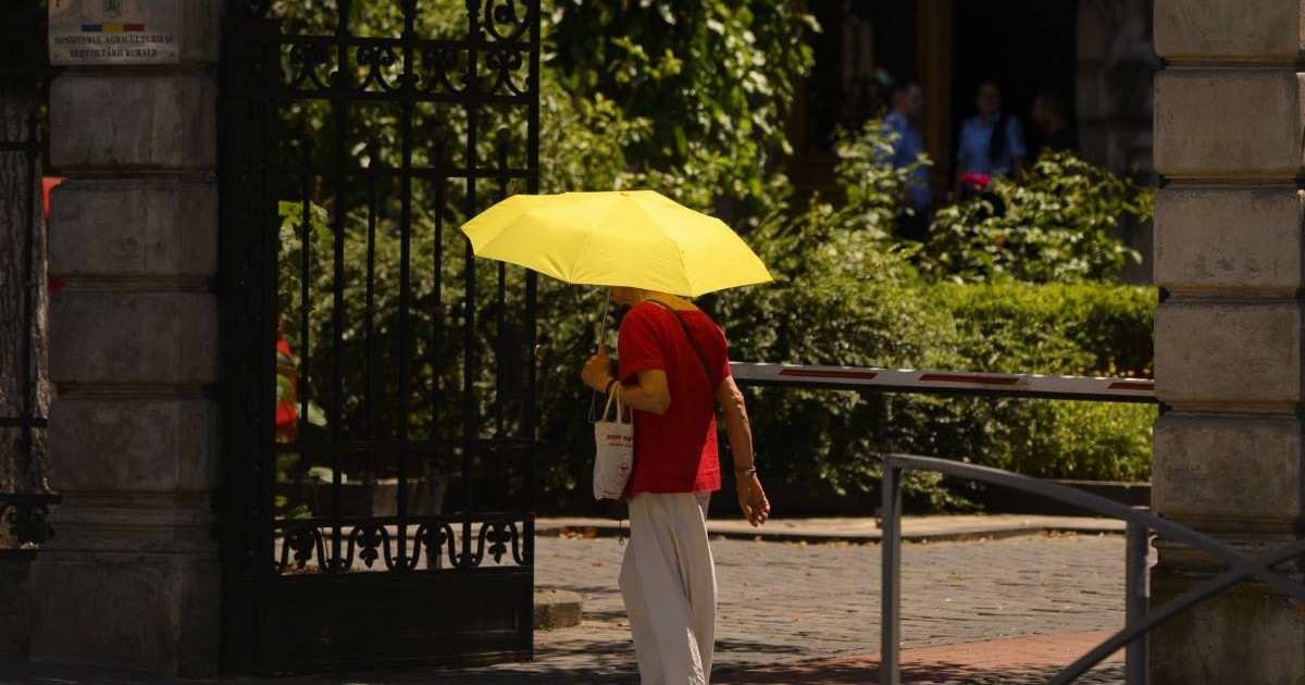 O femeie din București merge cu o umbrelă galben de soare pentru a se proteja de caniculă în mijlocul zilei