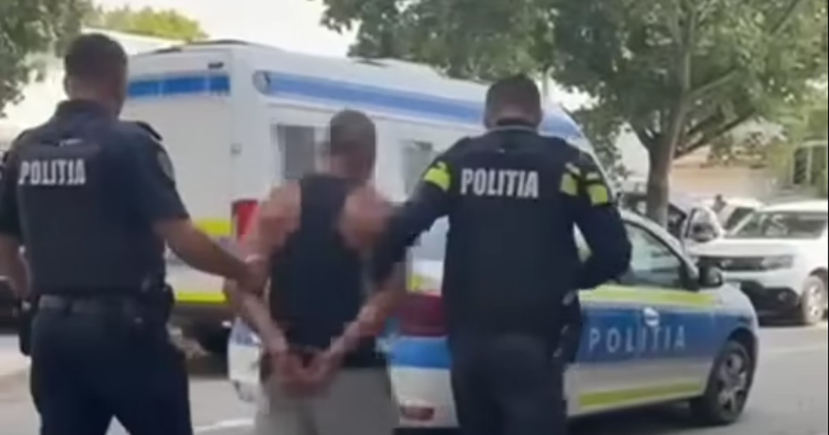 Un bărbat în maieu și pantaloni scurți având mâinile încătușate la spate este dus de doi polițiști către o autospecială de Poliție, septembrie 2025