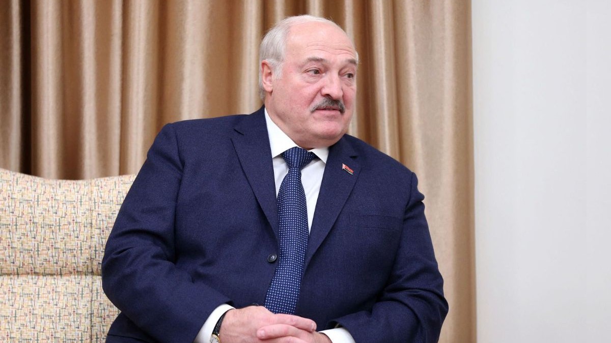 Aleksandr Lukașeko pe o canapea, îmbrăcat într-un costum bleumarin cu o cravată albastră și butoni batistp roșii