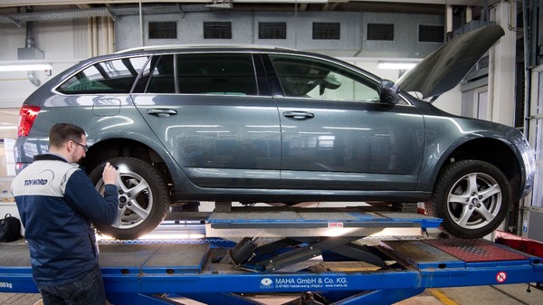 Un tehnician TÜV NORD inspectând roata din spate a unui autoturism Skoda Octavia Combi ridicat pe o platformă dintr-un atelier auto.
