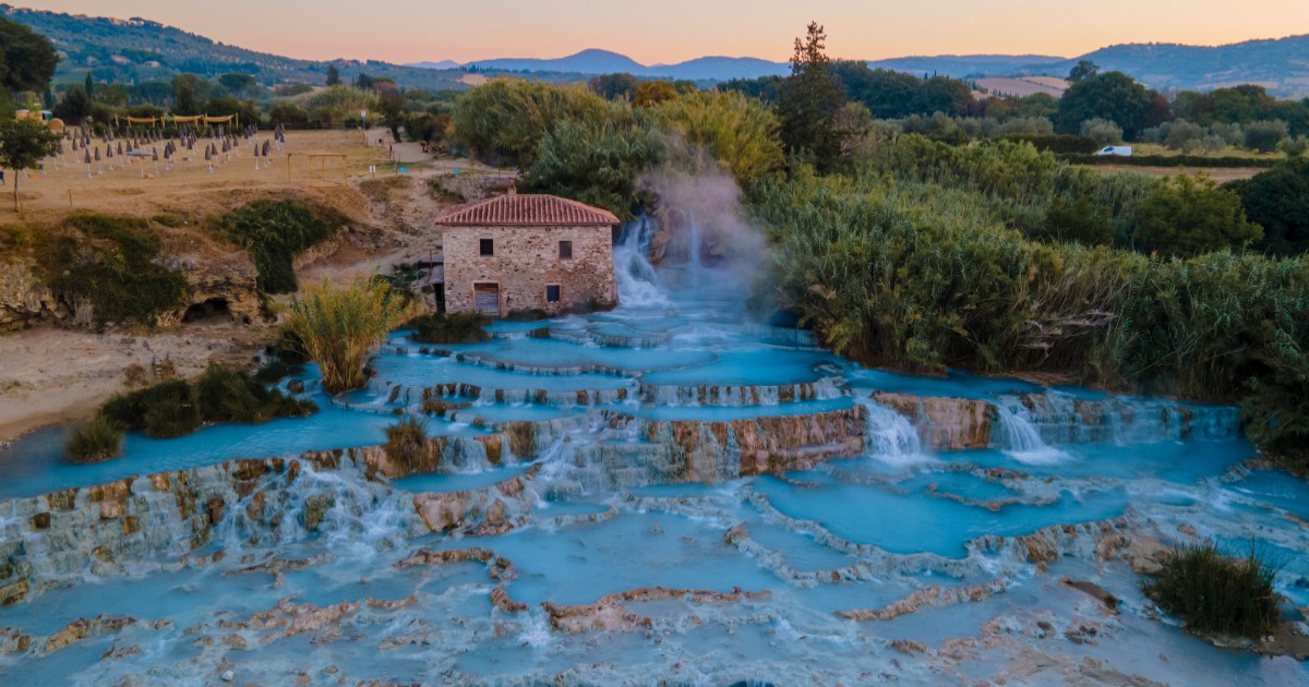 Vedere aeriană u Cascate del Mulino din Saturnia, Toscana. Cascade termale naturale cu bazine din travertin pline cu apă turcoaz, aburi calzi și o moară veche din piatră în fundal.