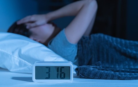 Tânără asiatică iritată, stresată, anxioasă, care suferă de insomnie, frustrată că stă trează în pat noaptea, cu dureri de cap sau migrene, cu probleme de sănătate, deranjată de zgomotul puternic, incapabilă să adoarmă.