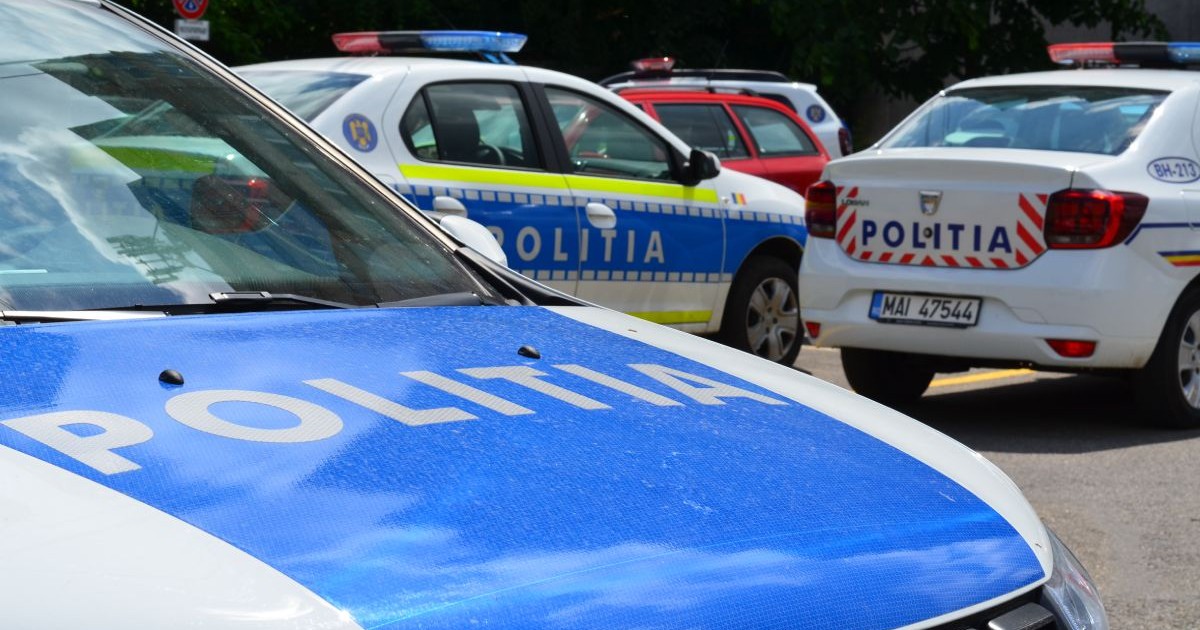 Imagine ilustrativă cu trei mașini ale Poliției Române, în prim plan capota albastră a uneia dintre ele pe care scrie POLITIA