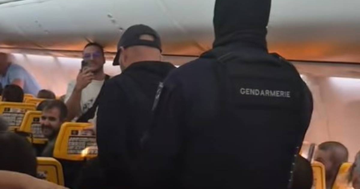 Un polițist mascat în timp ce duce în cătușe un bărbat pe culoarul avionului Ryanair