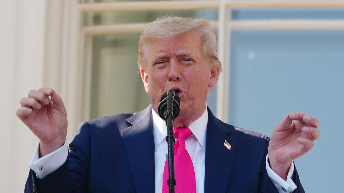Donald Trump surprins în timp ce vorbește la microfon, la Casa Albă, în iulie 2025. Poartă un sacou negru, o cămașă albă și o cravată roz. Liderul de la Casa Albă are mâinile ridicate