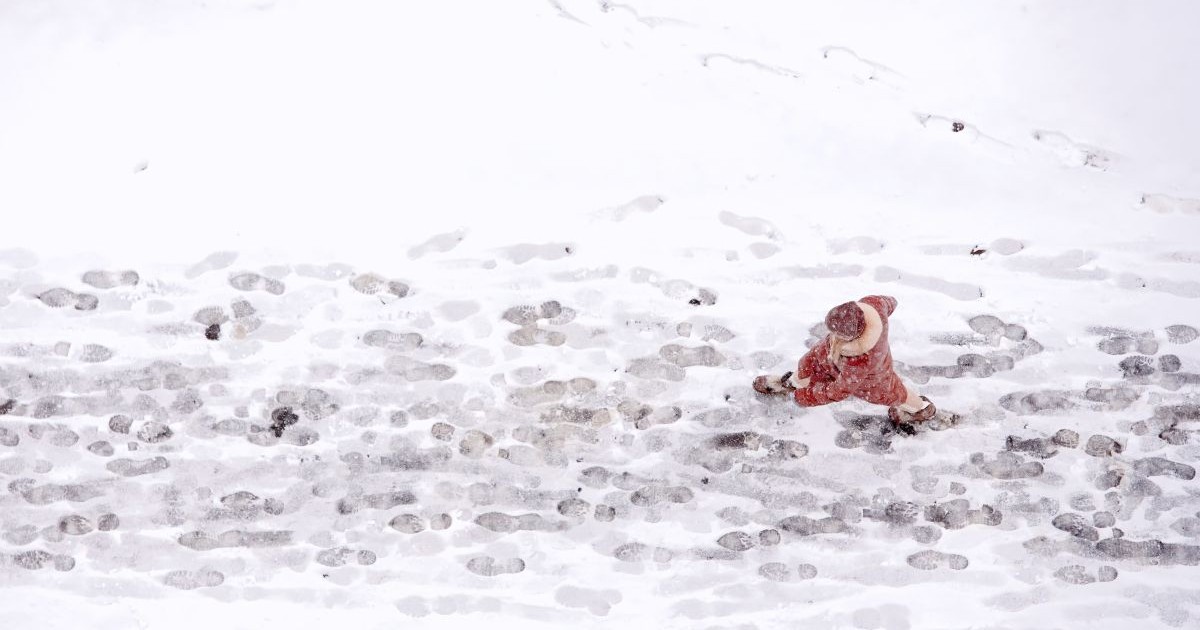 O femeie, fotografiată de sus, merge pe o stradă acoperită cu zăpadă, unde se văd urmele celor care au trecut, iar afară încă ninge. Foto: Shutterstock