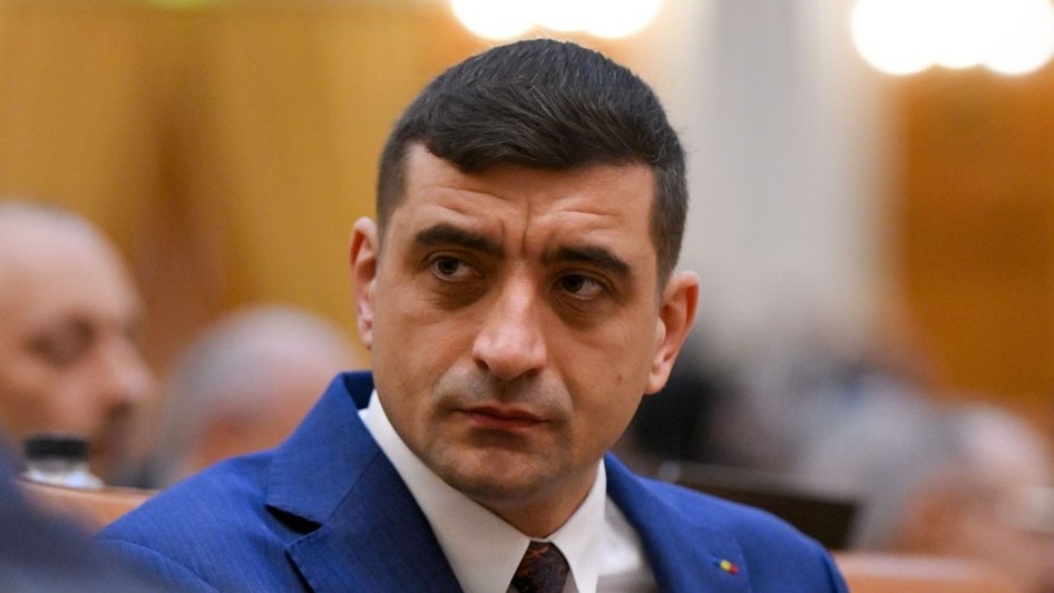 George Simion, îmbrăcat într-un costum albastru, cămașă albă și cravată neagră, în Parlament, pe fundal blurat, pe 26 aprilie 2026