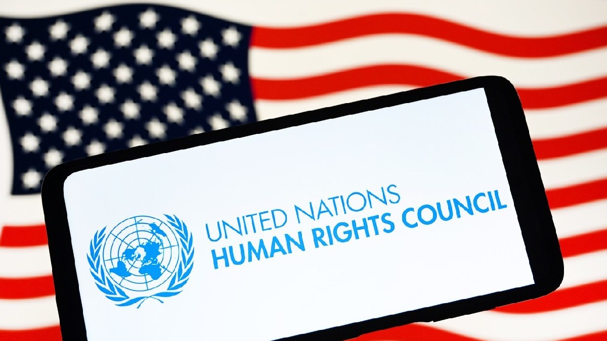 Logo-ul Consiliului Organizației Națiunilor Unite pentru Drepturile Omului (UNHRC) este văzut pe un smartphone și steagul SUA în fundal.