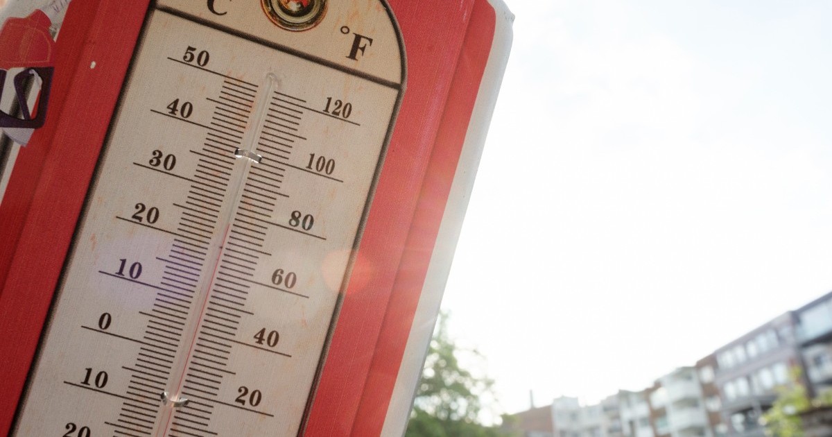 Un termometru de exterior în stil vintage, cu margine roșie, indicând o temperatură  de aproape 35°C în lumina soarelui.
