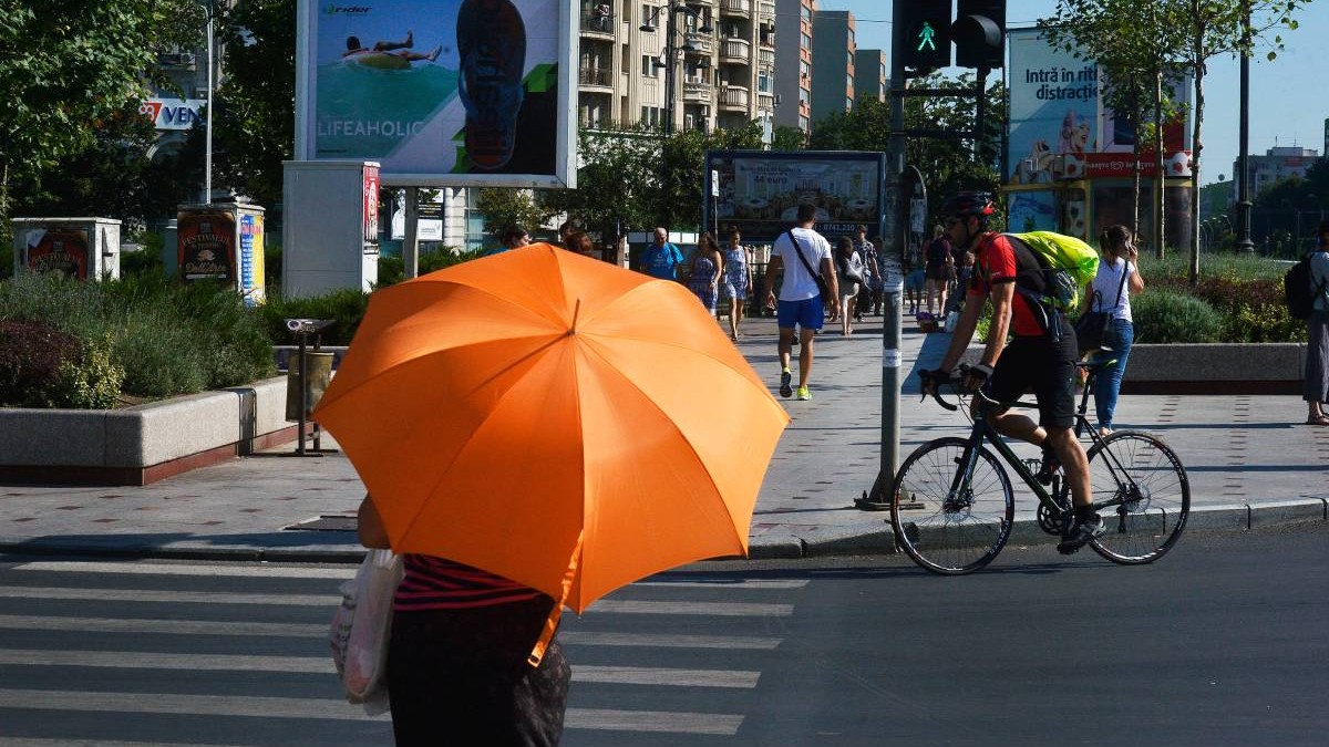 O femeie cu o umbrelă de protecție împotriva caniculei, pe stradă în București, într-o zi caldă de vară.