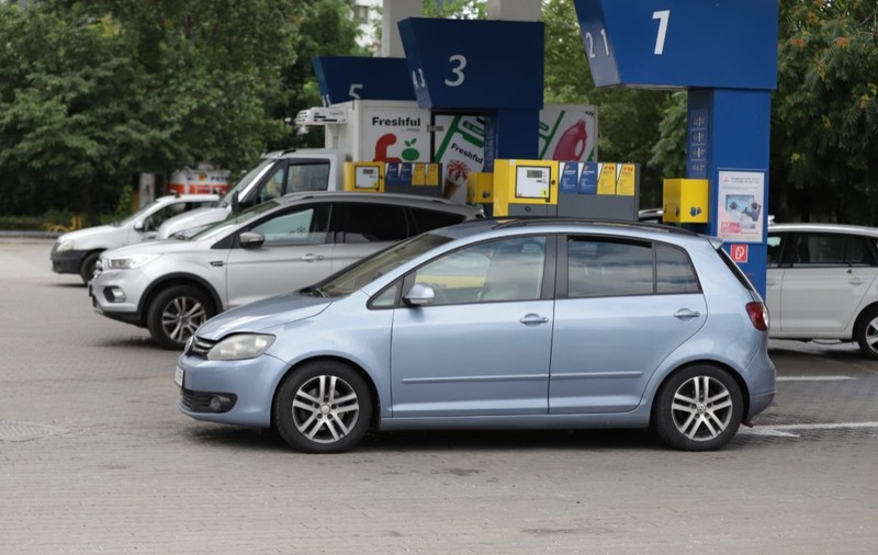Mai multe mașini parcate la pompele numerotate ale unei stații de carburanți, având în prim-plan un autoturism Volkswagen Golf