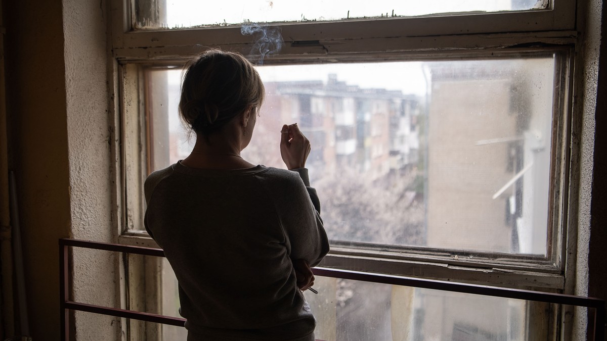 O femeie privește pe fereastră într-un bloc din Harkov, oraș bombardat de ruși încă din prima zi de război, 24 februarie. Foto: Profimedia