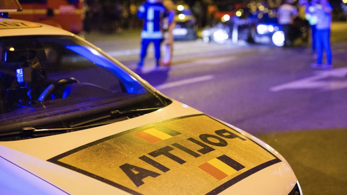 Fotografie în care în prim plan este o mașină a poliției, pe fundal agenți de poliție care fac măsurători în urma unui accident auto.