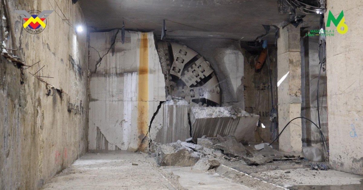 Imaginea surprinde momentul în care scutul de forare a străpuns peretele viitoarei stații de metrou Gara Băneasa, lăsând în urmă bucăți de beton și structuri dislocate. Se observă capul circular al utilajului TBM și interiorul masiv al construcției subterane, evidențiind amploarea lucrărilor de pe Magistrala 6.