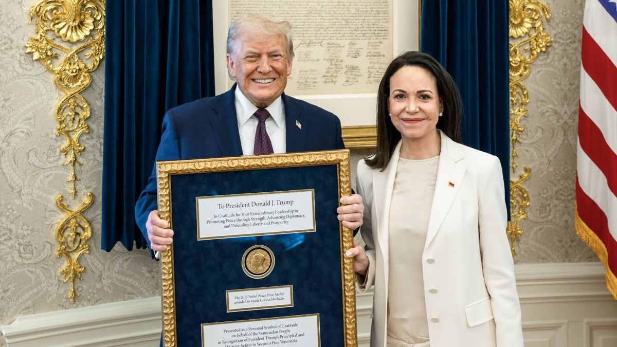 Donald Trump, stanga, in costum negru si cravata grena, rade fericit in timp ce pozeaza cu Premiul Nobel pentru pace de la Maria Corina Machado, dreapra, in costul alb, cu parul desfacut,. Machado, câstigatoarea prestigiosului premiu, i l-a oferit cadou liderului de la Casa Alba, 15 ianuarie 2026