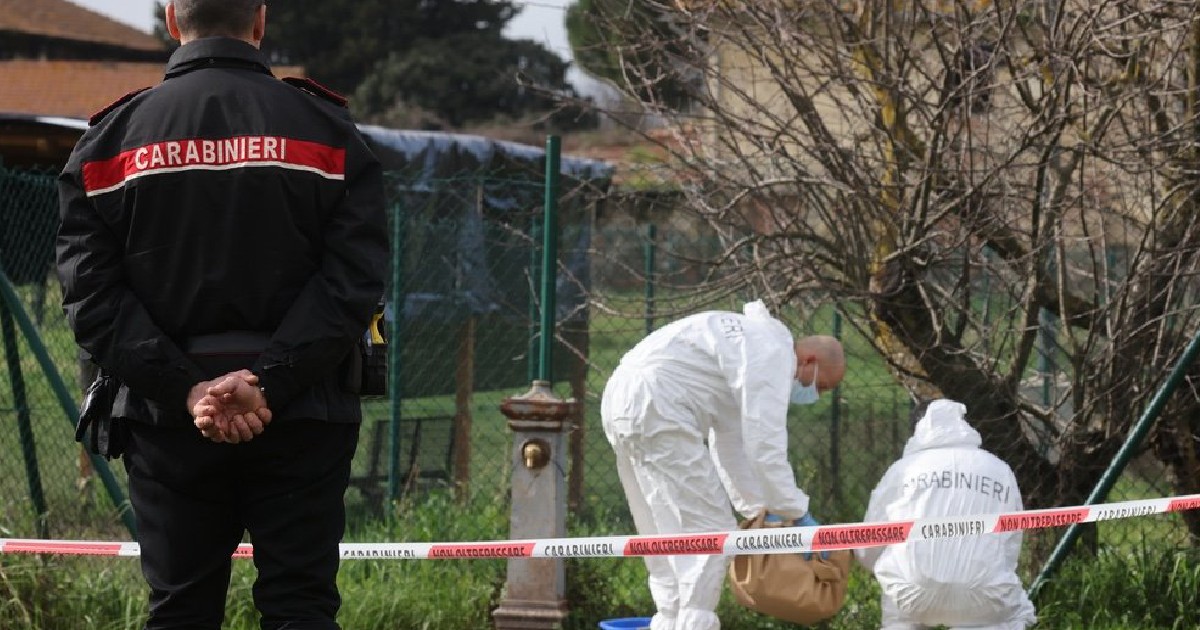 Imaginea surprinde o scenă de investigație desfășurată de autoritățile italiene: în prim-plan este un carabinier stând cu spatele, iar în plan secund, doi anchetatori echipați în costume albe de protecție lucrează la nivelul solului, lângă niște tufișuri. Zona este delimitată de o bandă de avertizare.