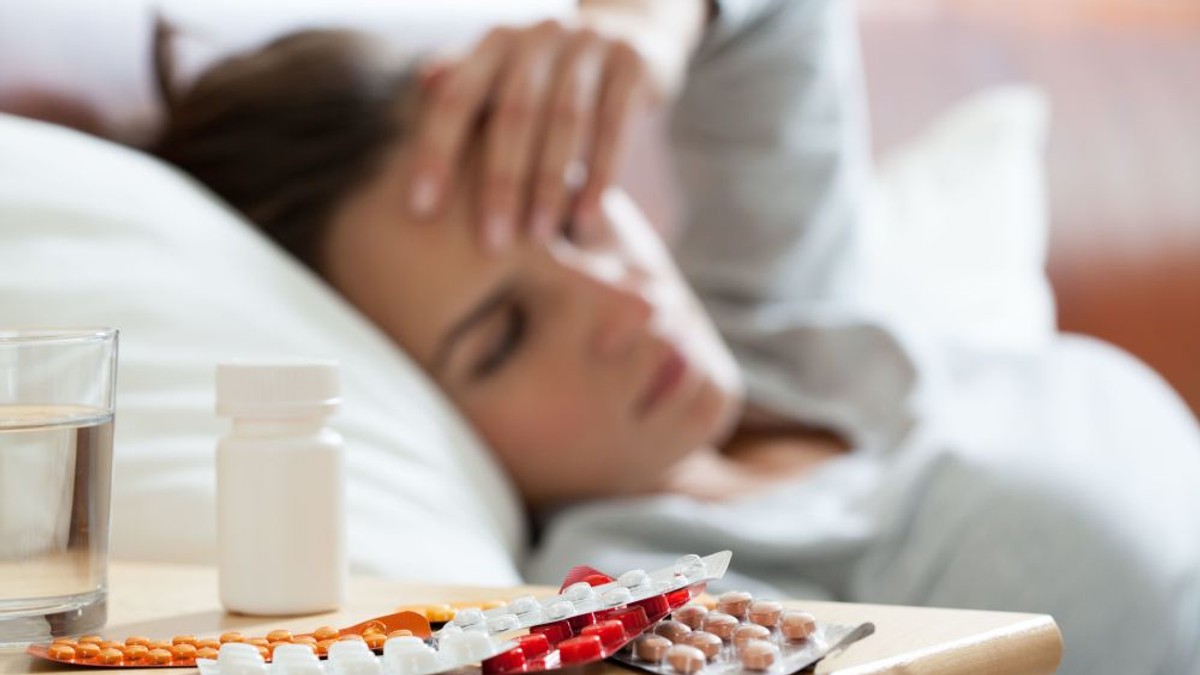 27 de decese, din cauza gripei. O femeie răcită, care își pune mâna pe frunte. Alături, pe un dulăpior sunt multe medicamente