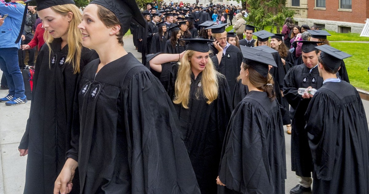 Mai mulți tineri, cu șepci și halate de absolvire de la Universitatea Harvard urca niște trepte.