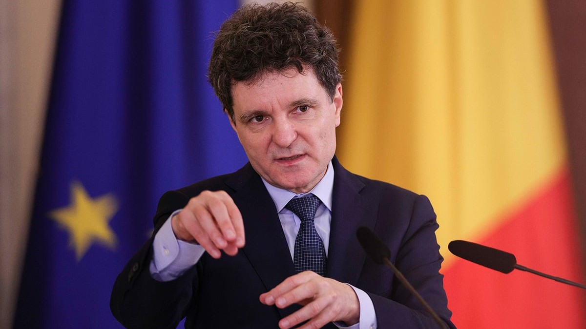 Nicușor Dan îmbrăcat într-un costum negru, cămașă bleu, cravată neagră cu mici puncte albe, explică ceva arătând cu mâinile.
