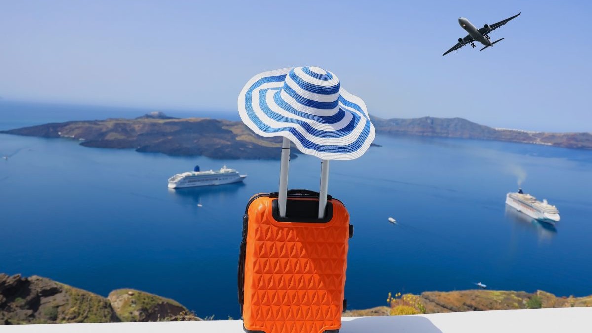 Concept de vară cu bagaje portocalii, pălărie și priveliște asupra orașului Oia de pe insula Santorini din Grecia