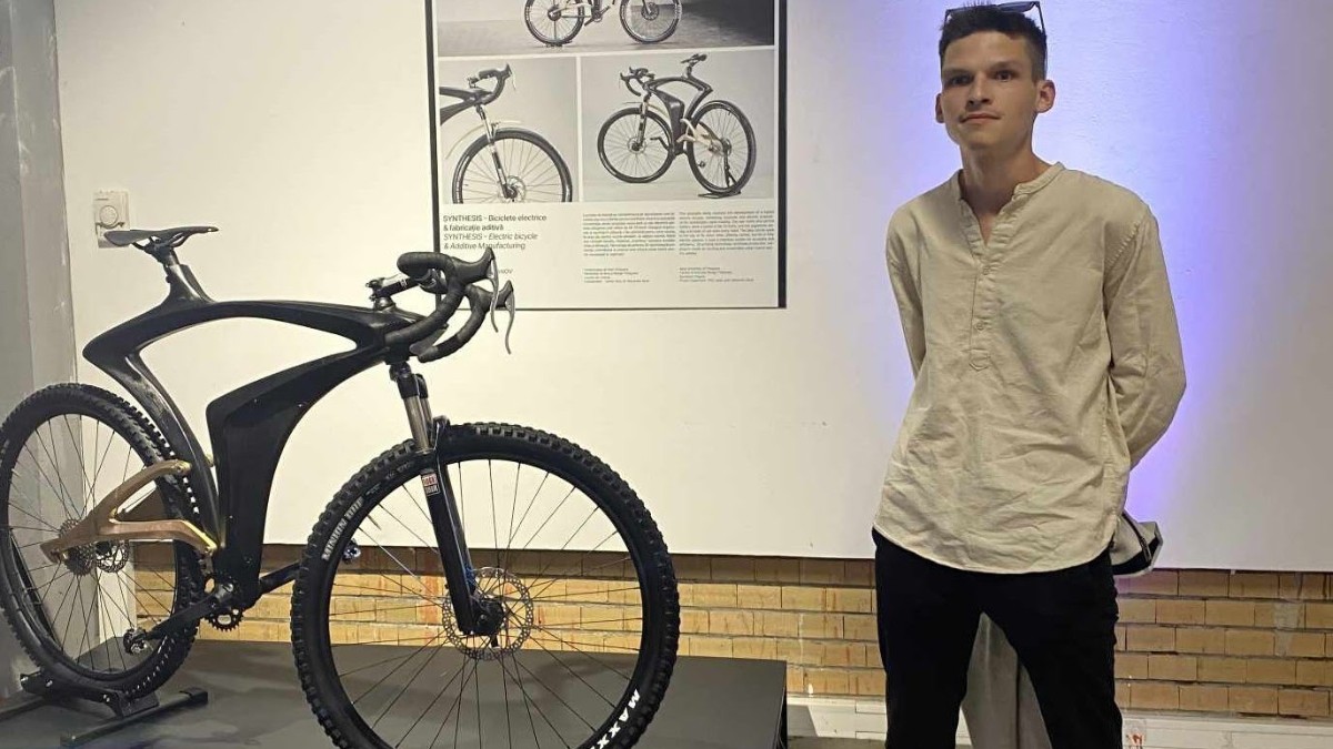 David Borovci îmbrăcat în cămașă albă și blugi negri, cu ochelari pe cap, lângă o bicicletă