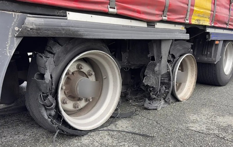 Partea inferioară a unei remorci de camion ale cărei anvelope sunt sever deteriorate și sfâșiate, lăsând jantele expuse direct pe carosabil.