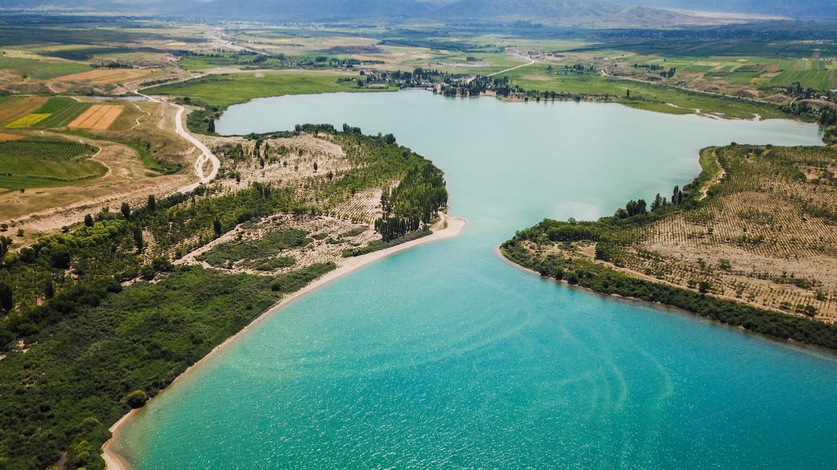 Imagine aeriană cu lacul Issyk-Kul din Kirghizistan, cu apă turcoaz, înconjurat de păduri.