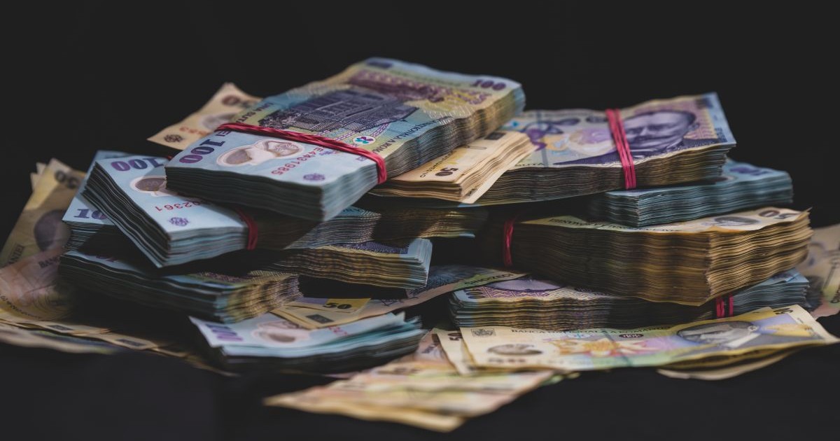 Teancuri de bancnote de 100 de lei și 50 de lei, legate de elastice de culoare roșie, pe fundal negru