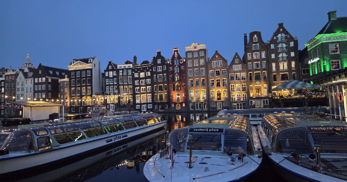 Bărci, canal pe strada Damrak, din Amsterdam, Olanda, pe înserat, în spate se văd casele tipice, martie 2025