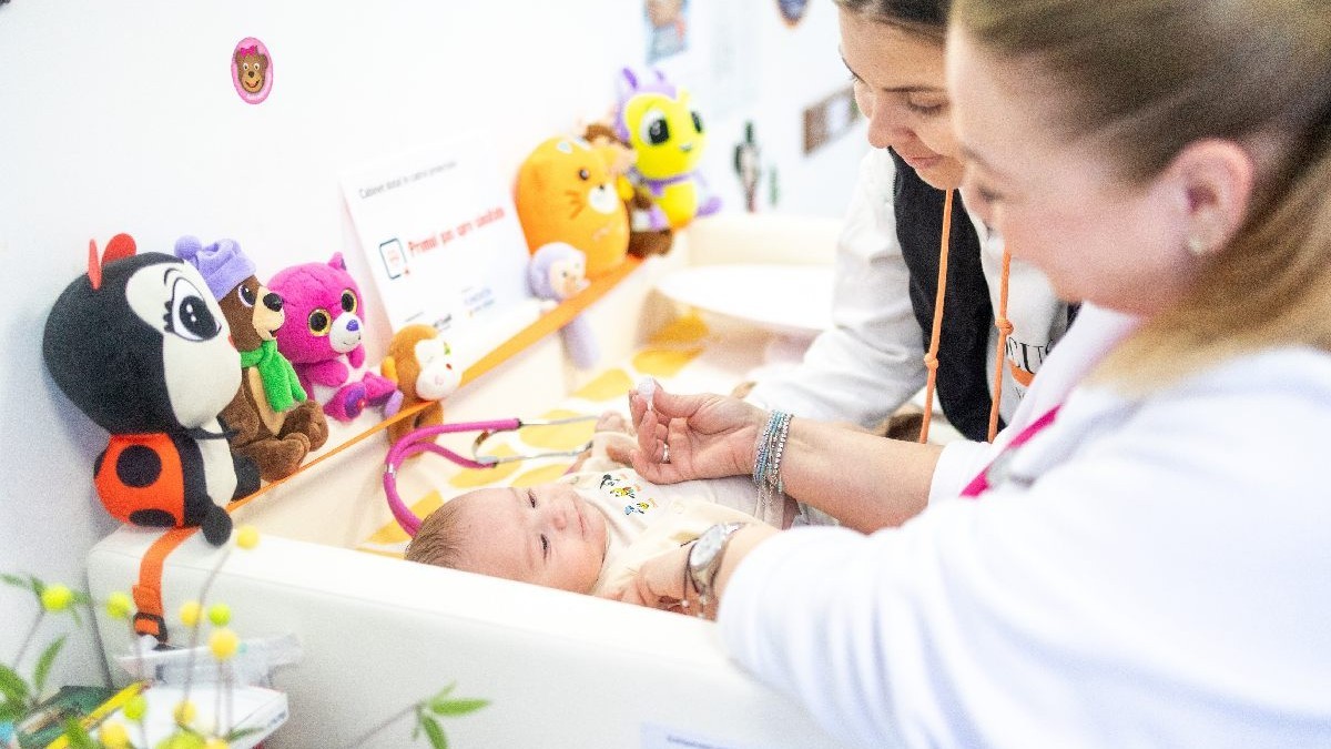 Un bebelus intr-o cutie patut, consultat de medic, cu mama langa el.Pacientul din rural nu are acces suficient la servicii De ce lasă medicii de familie satele din România