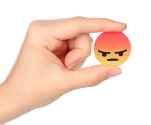 Kiev, Ukraine - September 04, 2017: Hand holds Facebook Angry Empathetic Emoji Reaction, printed on paper. Facebook is a well-known social networking service