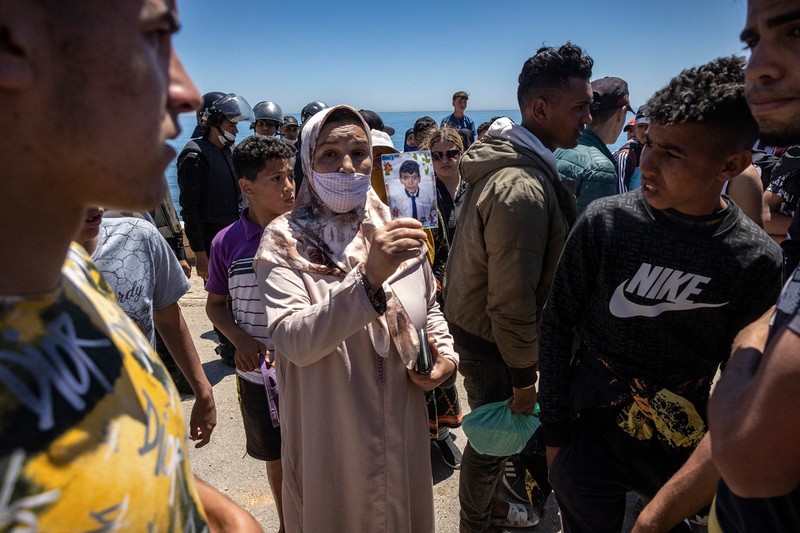 O femeie arată o fotografie a fiului ei, pe care-l caută, către migranții adunați pe o plajă din Fnideq. Foto: Profimedia Images