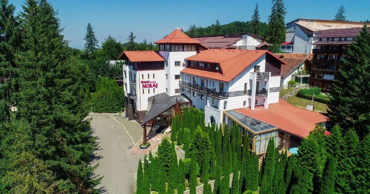 Hotelul Miraj din Poiana Brașov, cladire alba, cu acoperișuri de țiglă roșie, și curte 