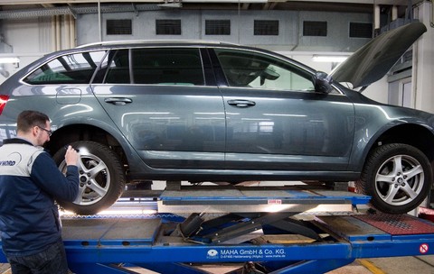 Un tehnician TÜV NORD inspectând roata din spate a unui autoturism Skoda Octavia Combi ridicat pe o platformă dintr-un atelier auto.