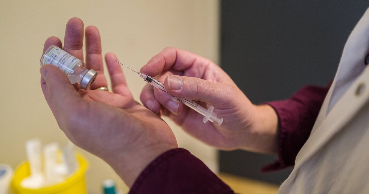 în imagine se văd două mâini, în stânga este ținut serul de vaccin și în dreapta este ținută siringa