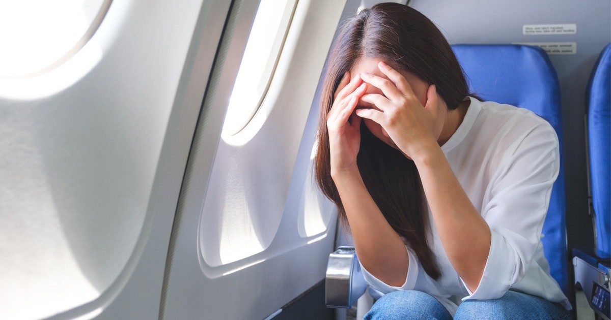 O femeie imbracata in camasa alba si blugi sta cu mainile la cap intr-un avion. Hipoxie si atac de panica la bord. Foto Imago