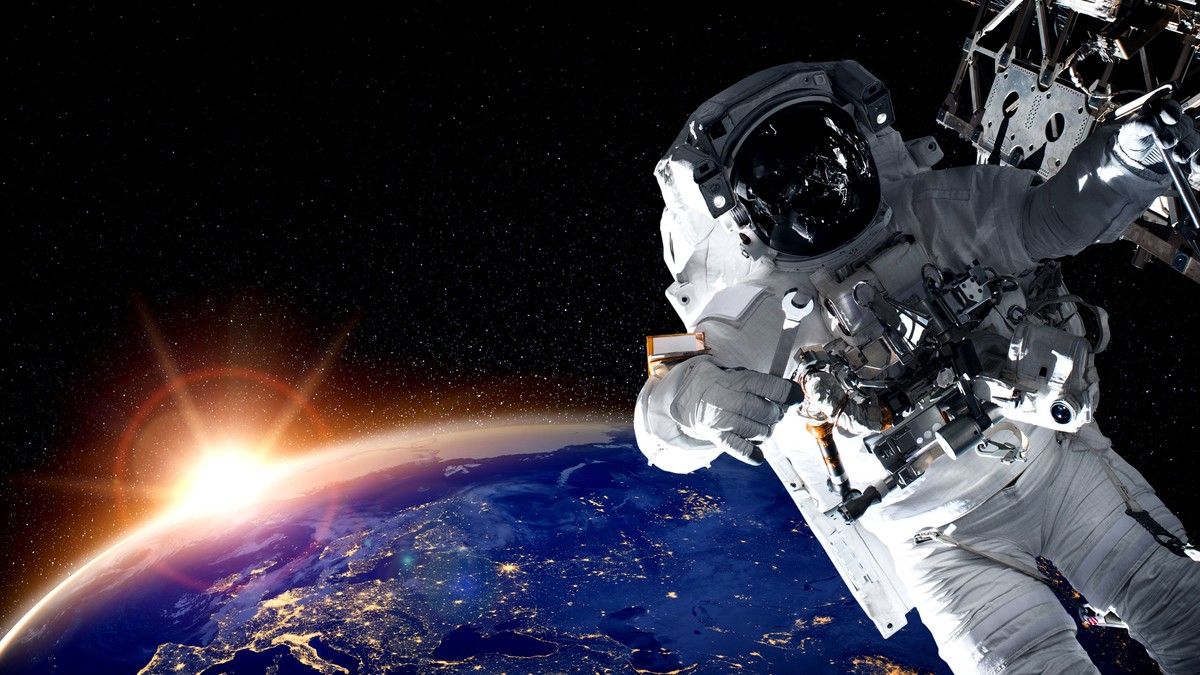 De ce se antrenează cosmonauții în apă - Imagine cu un cosmonaut care efectuează o intervenţie tehnică în spaţiul cosmic, având în fundal Pământul şi Soarele.