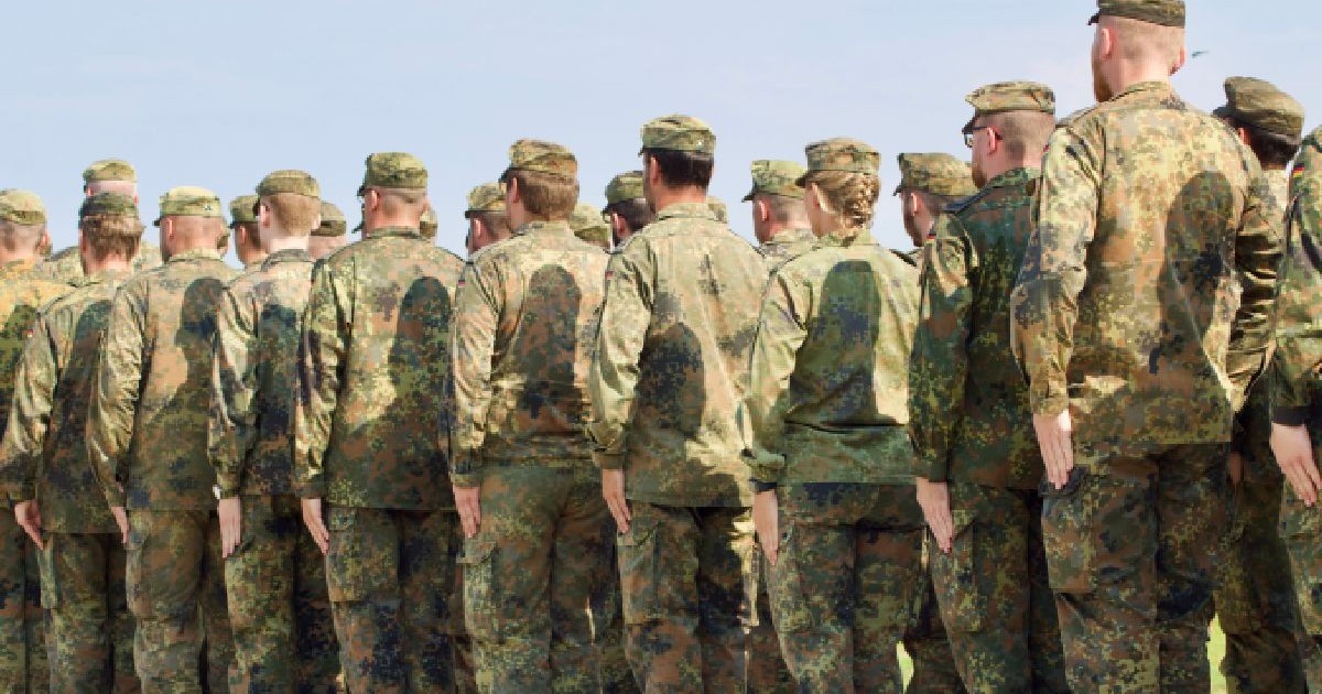Fotografie cu un grup de soldați în uniforme de camuflaj, aliniați în formație, sub un cer senin și albastru.