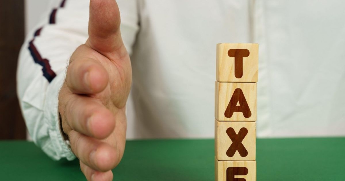 Pe o suprafață verde, sunt patru cuburi cu inscripția Taxe, iar alături este mâna unui bărbat.