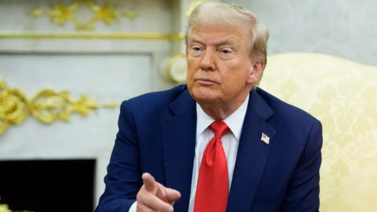 Donald Trump în sacou negru, cămașă albă și cravată roșie, în timp ce stă pe scaun