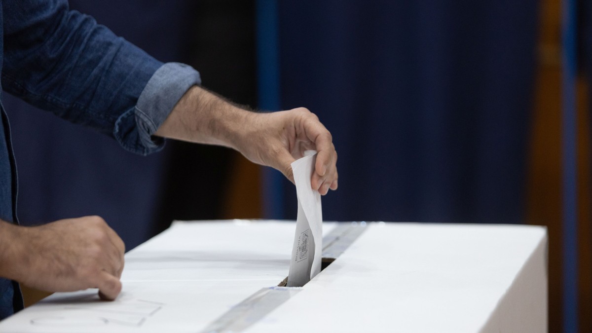 Un bărbat cu jachetă albastră care introduce buletinul de vot în urnă, într-o secție de votare