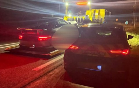 O mașină pe care scrie Gendarmerie oprită pe marginea drumului lângă o platformă de tractare pe care se află o mașină neagră