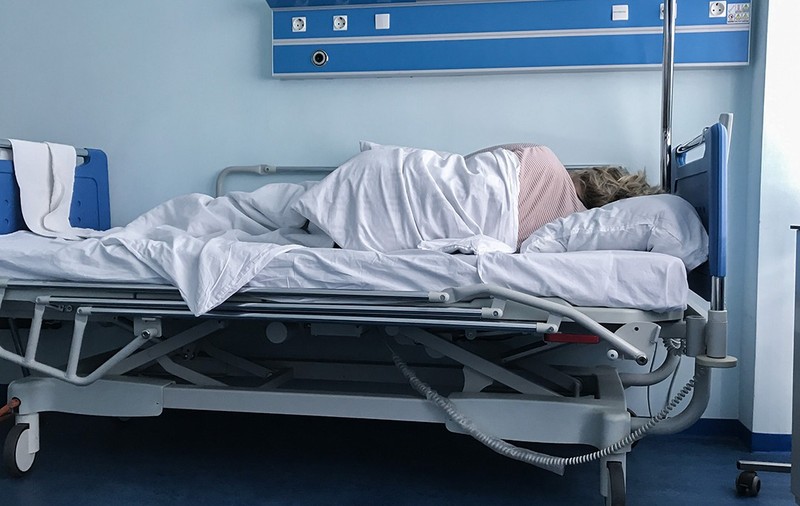 O femeie cu spatele într-un pat din spital