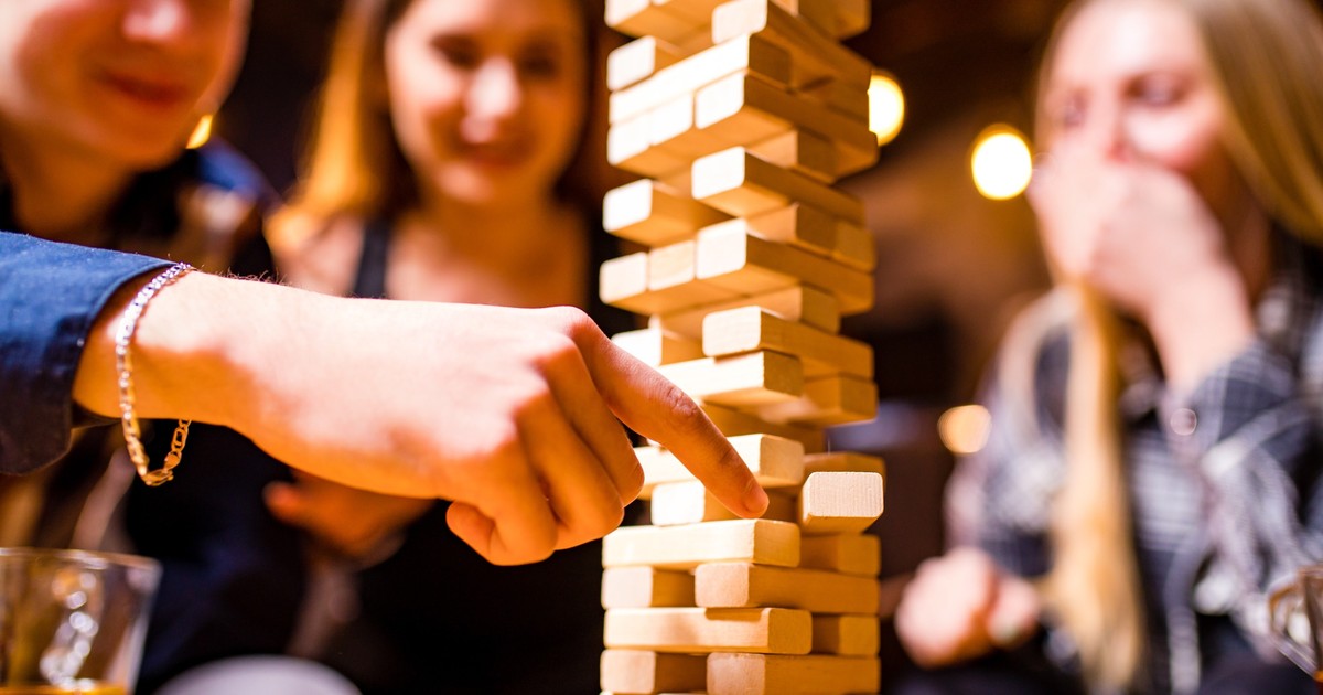 Cum se joacă Jenga – reguli și variante de joc - Imagine cu trei tinere care joacă Jenga