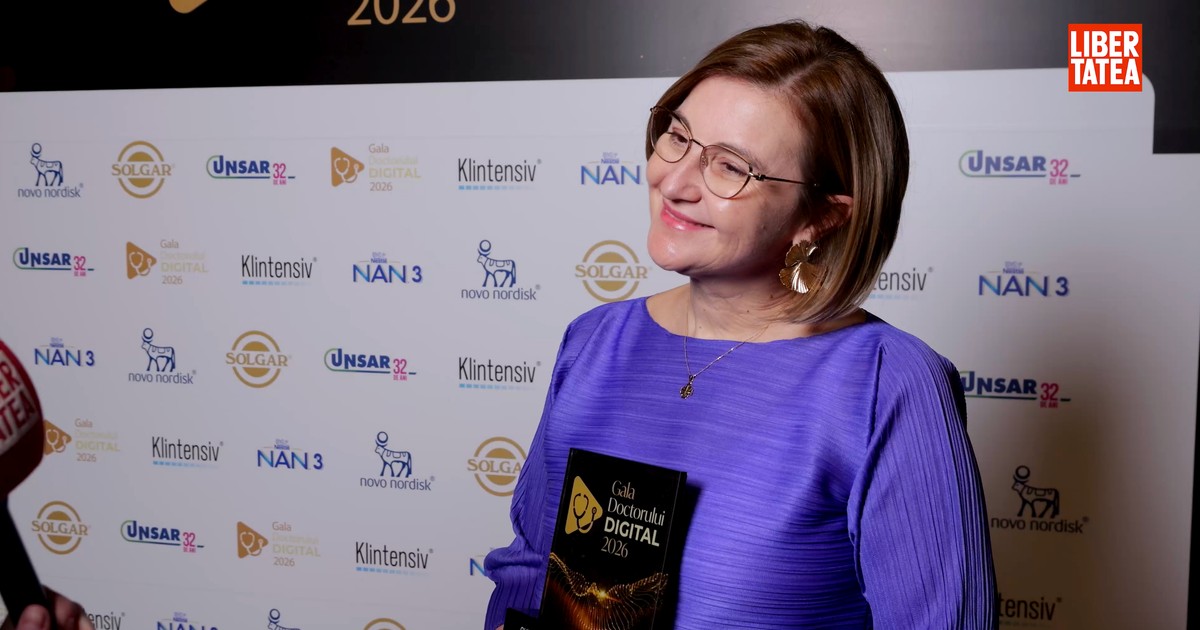Dr. Ina Petrescu, medic primar chirurgie plastică, la Gala Doctorului Digital 2026, îmbrăcată cu o rochie mov, pe un fundal cu un panou alb.