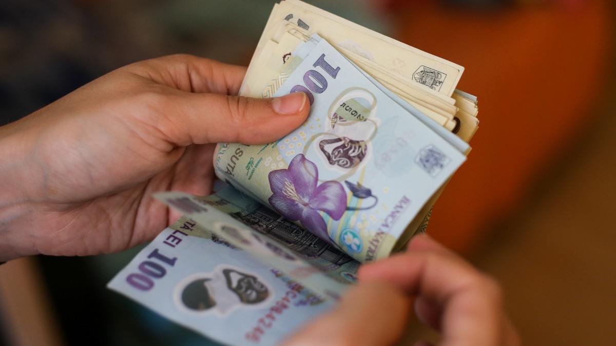 Un bărbat care numără bani și ține hârtii de 50 și 100 de lei în mână